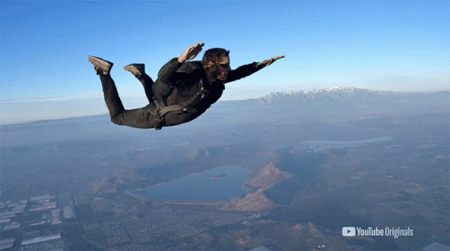 Skydiver descending against a clear blue sky above mountains and water.